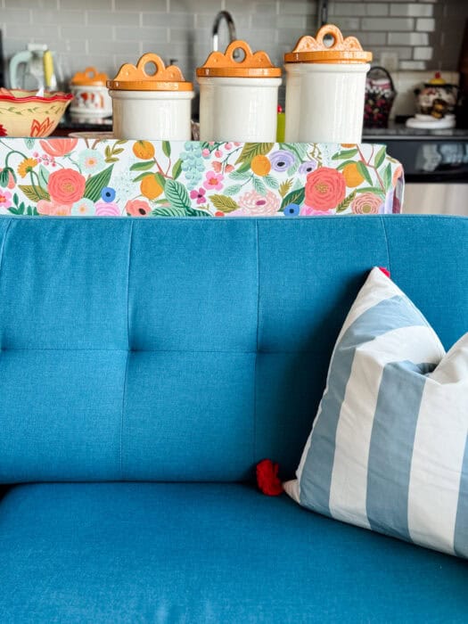 Close-up with sofa – Wallpapered sideboard styled behind teal sofa with striped pillow.