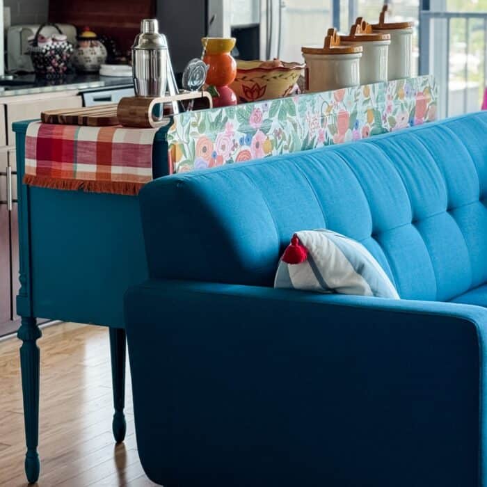 Close-up with sofa – Wallpapered sideboard styled behind teal sofa with striped pillow.