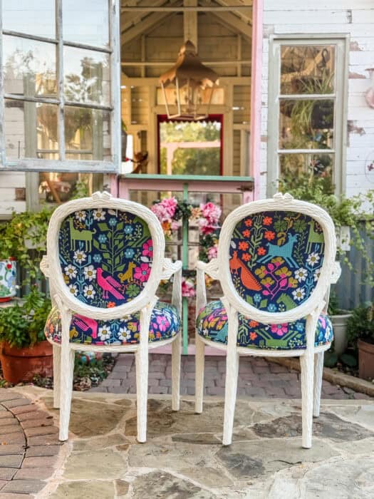 Two blue embroidered chairs in with colorful designs and white paint.