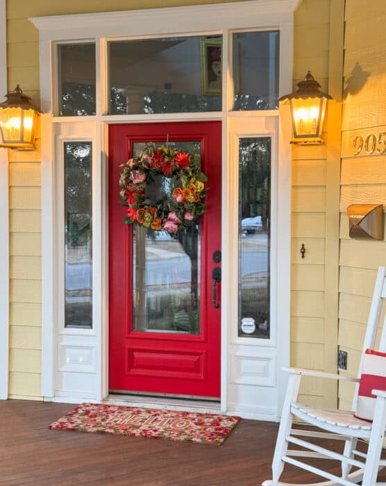 Regal red front door with brass light sconces and colorful rug