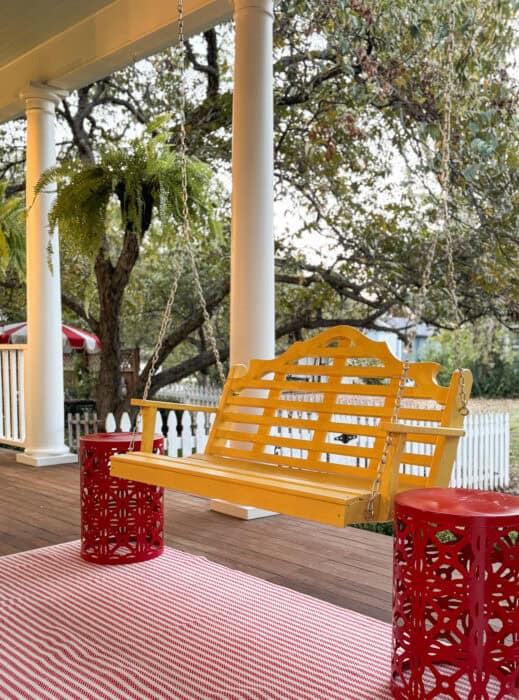 Yellow house porch with red door, mustard swing, and Annie Selke rug