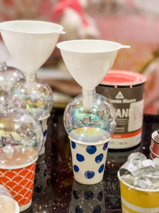 Painted ornaments drying upside down on small cups as excess paint drains out.