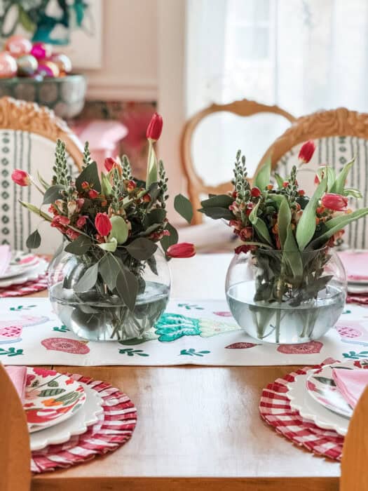 Christmas dining table with red gingham placemats, pink vintage napkins, and a simple flower arrangement of tulips, snapdragons, and greenery.