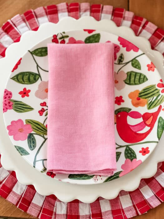 Christmas dining table with red gingham placemats, pink vintage napkins, and a simple flower arrangement of tulips, snapdragons, and greenery.