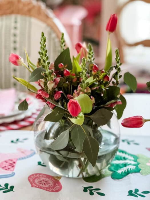 Pink tulips, snapdragons, and greenery arranged in a glass vase as a simple Christmas dining room centerpiece.