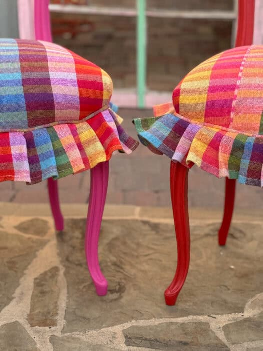 Picture of pink painted leg of a chair and a red painted leg of a chair with a plaid seat and ruffle around the edge. 