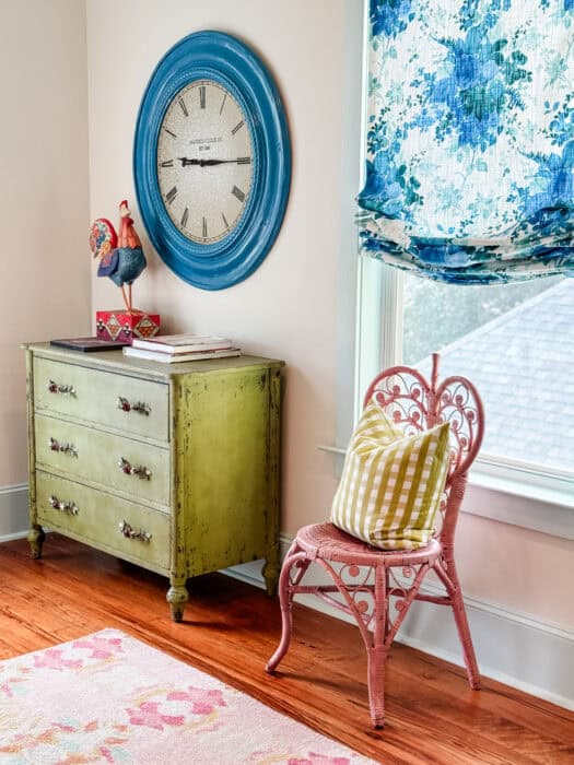 Blue painted clock above a green dresser and a pink chair.