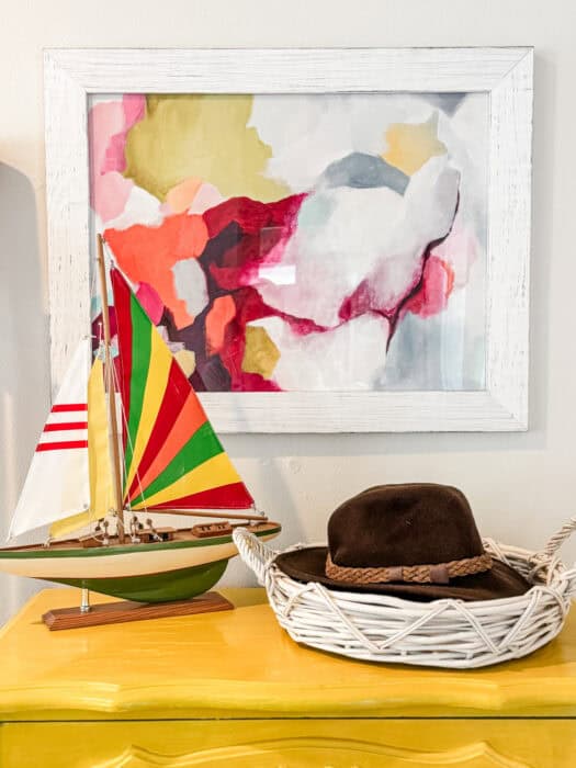 Abstract art with a sailboat and hat on dresser.