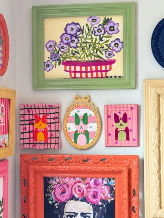 Frames and prints in a variety of colors hung on a wall. 