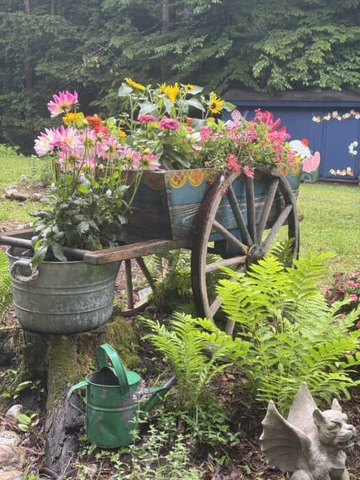 Flea market garden decor ideas including an antique wagon planter, painted chair, and vintage buckets in a cottage garden