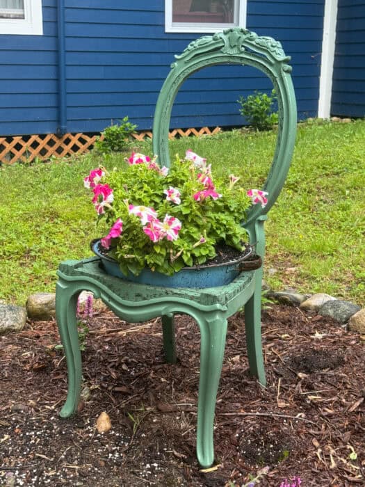 Hand painted vintage chair used as a garden accent holding a metal pot of flowers in a cottage garden