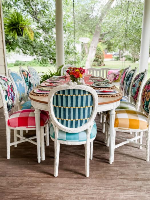 Multi-colorful chairs at a table on a porch.