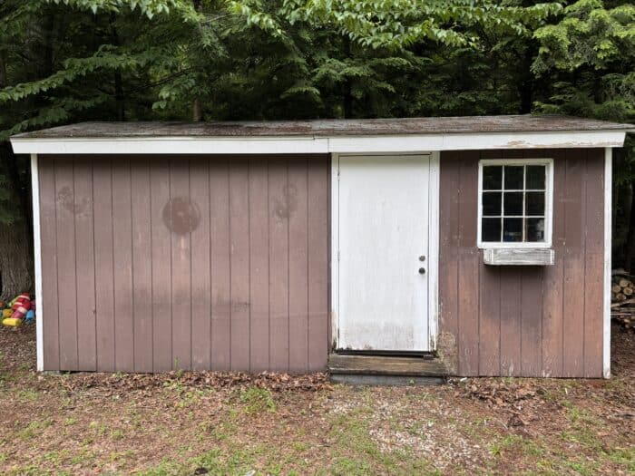 Small brown shed with white trim before makeover.