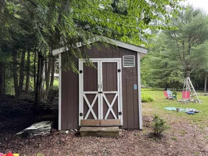 Small brown shed with white trim before makeover.