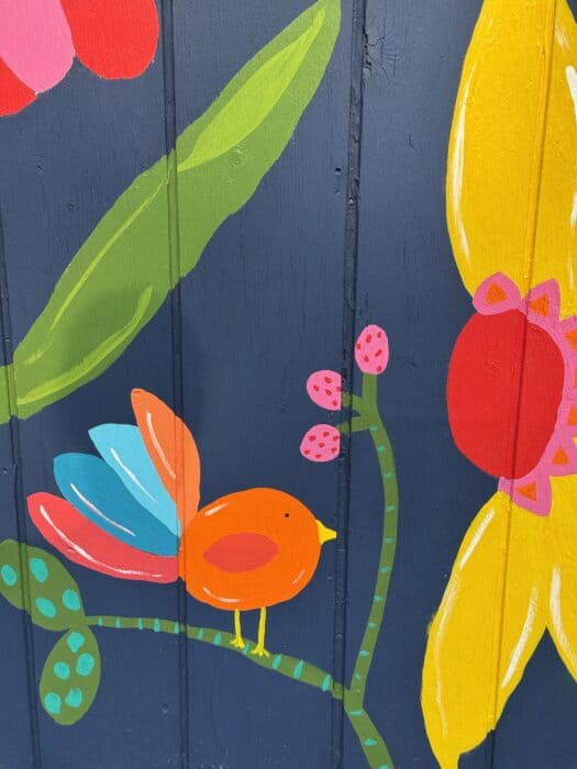 Navy shed covered in oversized, colorful flowers, butterflies, daisies, and gingham accents.