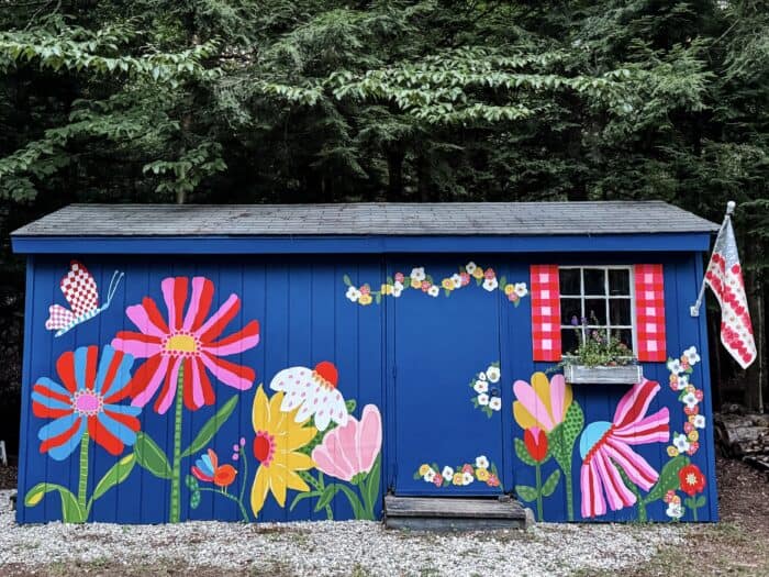Navy shed covered in oversized, colorful flowers, butterflies, daisies, and gingham accents.