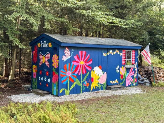 Navy shed covered in oversized, colorful flowers, butterflies, daisies, and gingham accents.