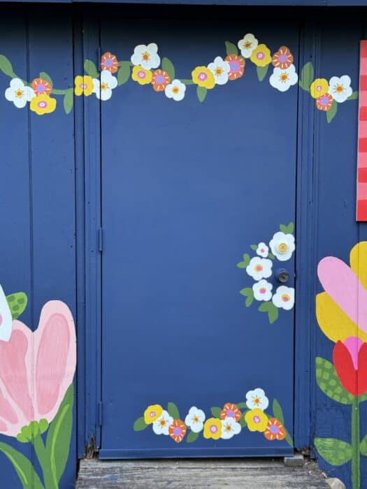 Navy shed covered in oversized, colorful flowers, butterflies, daisies, and gingham accents.