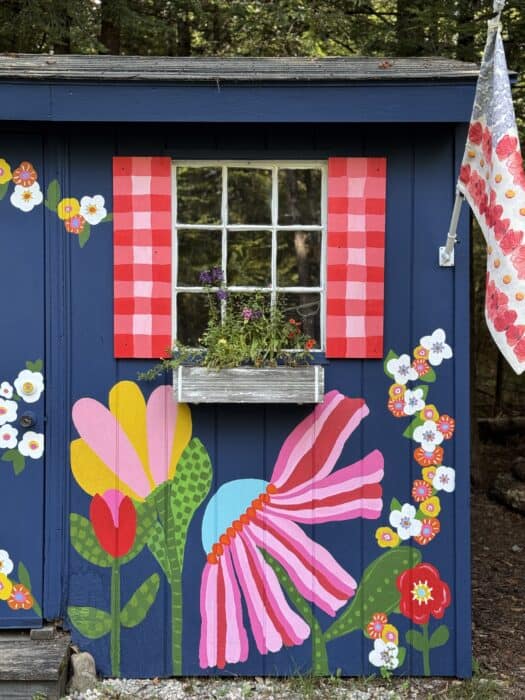 Navy shed covered in oversized, colorful flowers, butterflies, daisies, and gingham accents.