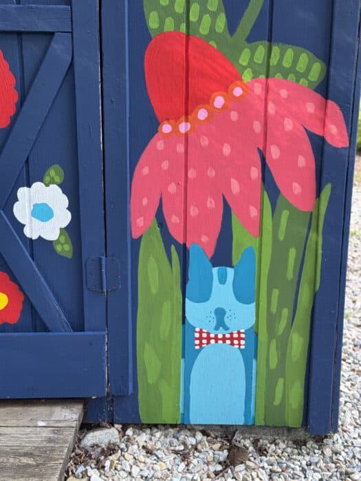 Navy shed covered in oversized, colorful flowers, butterflies, daisies, and gingham accents.