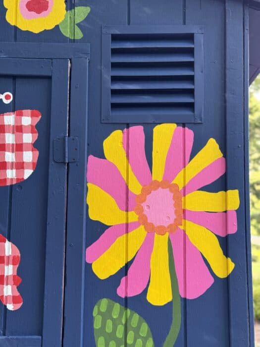 Navy shed covered in oversized, colorful flowers, butterflies, daisies, and gingham accents.