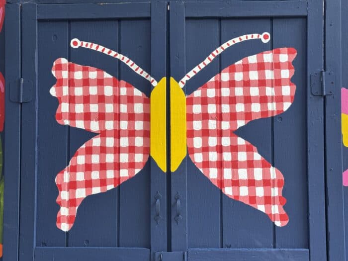 Navy shed covered in oversized, colorful flowers, butterflies, daisies, and gingham accents.