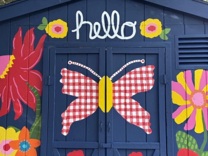 Navy shed covered in oversized, colorful flowers, butterflies, daisies, and gingham accents.