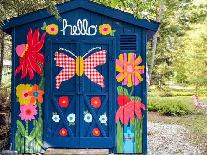 Navy shed covered in oversized, colorful flowers, butterflies, daisies, and gingham accents.