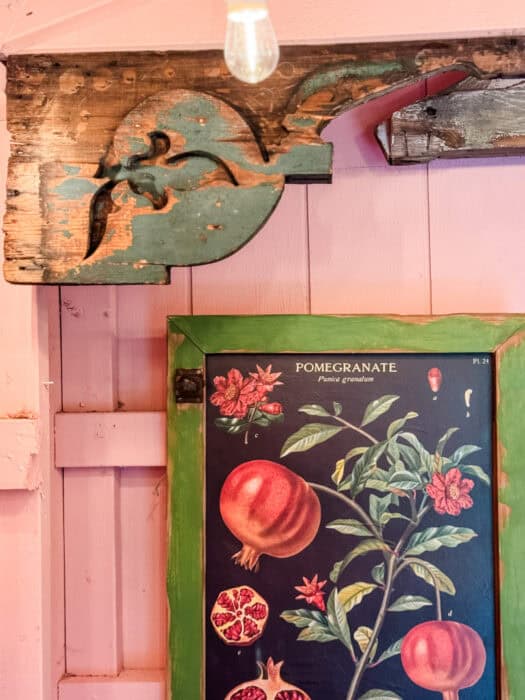 Pink shed interior with vintage botanical art, gingham wreath, and warm battery string lights.