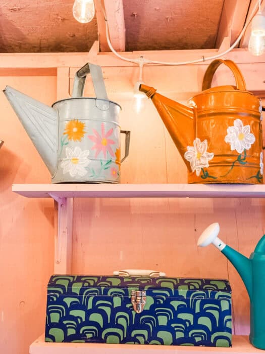DIY shed workspace with pink walls, salvaged decor, vinyl plank floor, and garden tools nearby.