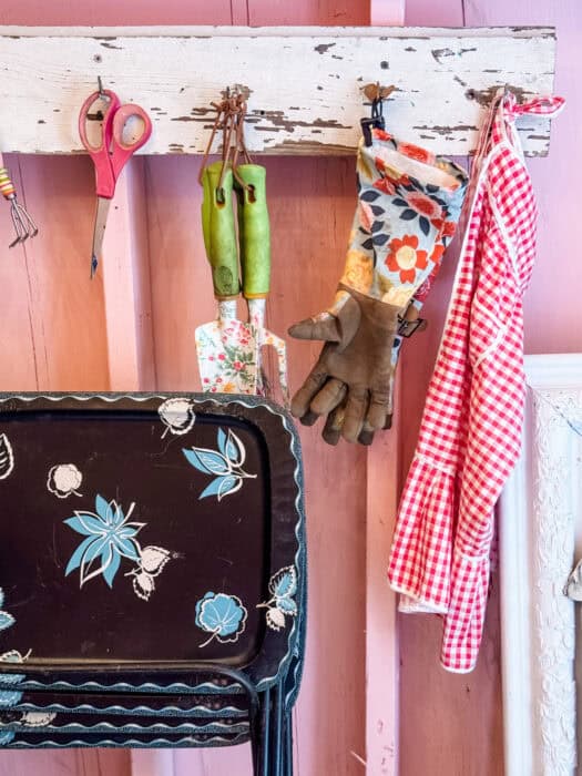 DIY shed workspace with pink walls, salvaged decor, vinyl plank floor, and garden tools nearby.