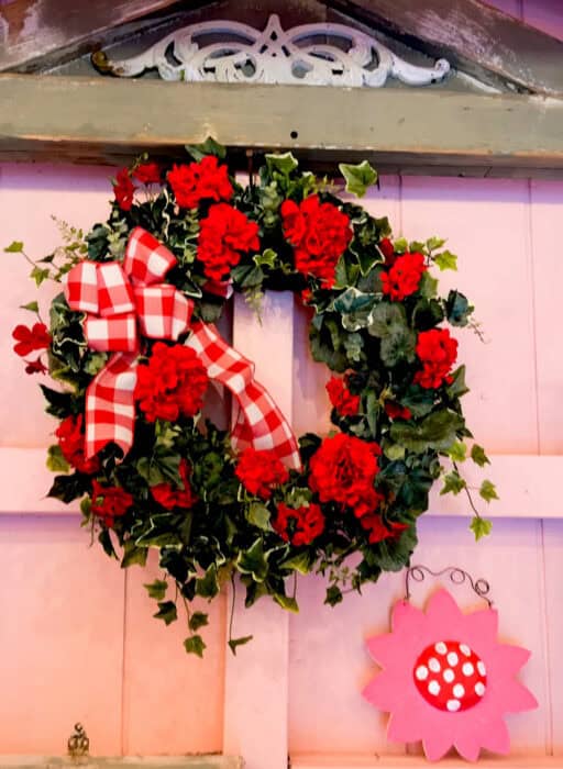 Pink shed interior with vintage botanical art, gingham wreath, and warm battery string lights.