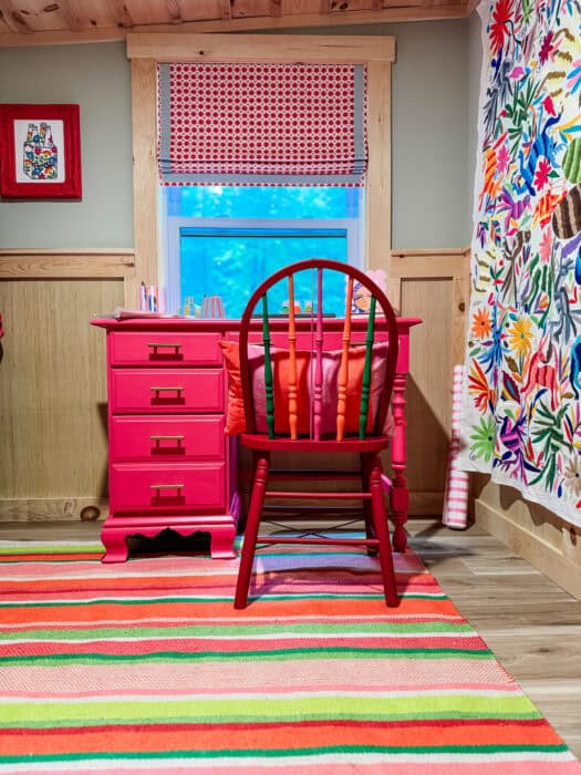 Colorful closet office with pink desk, striped rug, and embroidered curtain