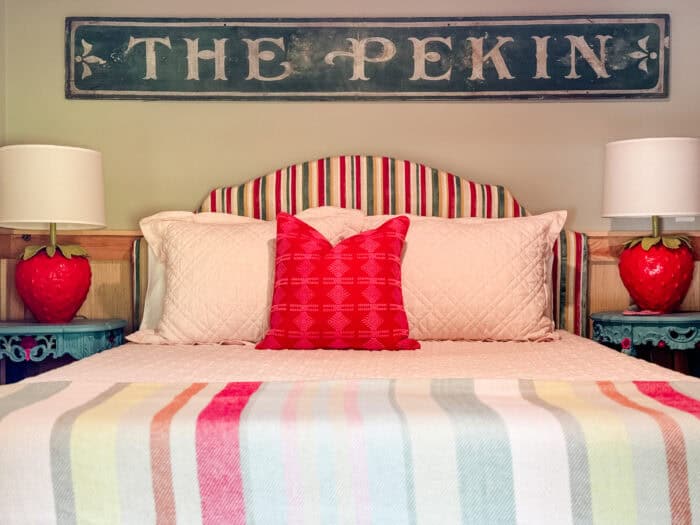 Striped headboard with red pillow and strawberry lamps in colorful cabin bedroom